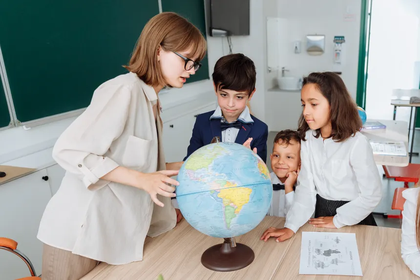 A teacher and three students engaged in a geography lesson, examining a globe in a classroom setting.