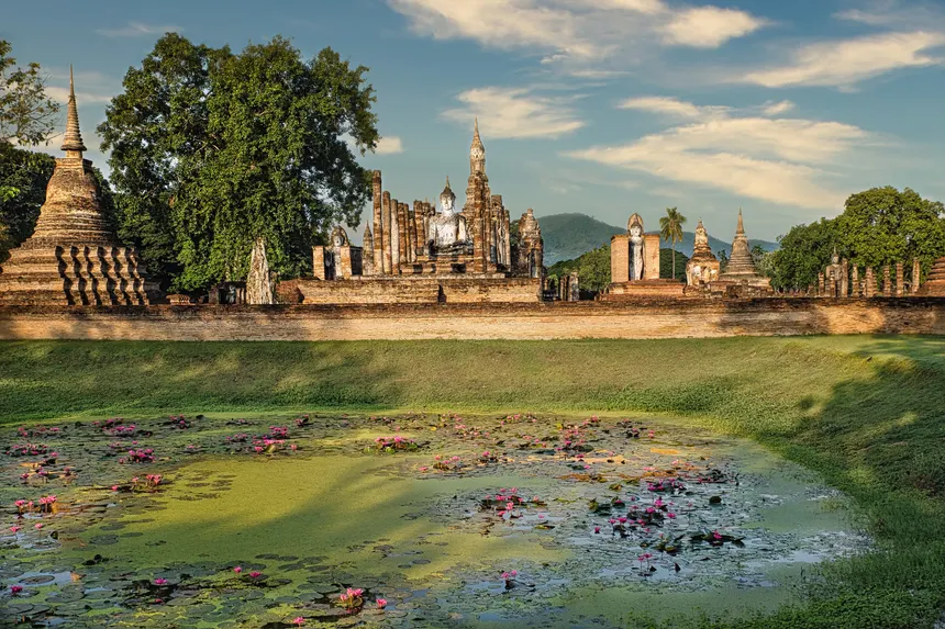Serene view of ancient temples and blooming lotus pond in Sukhothai, Thailand.