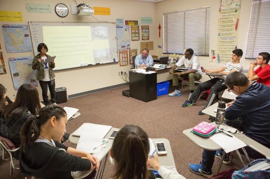 A diverse group of students in a classroom participating in a lesson with an educator.