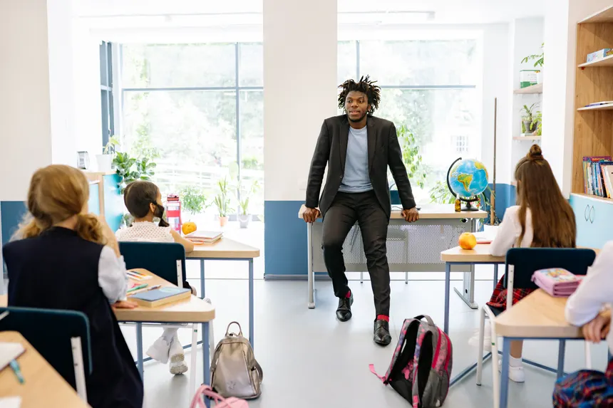 A teacher engages with students in a bright, modern classroom setting, promoting education.