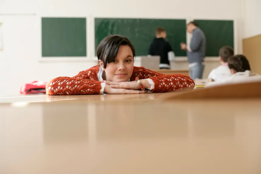 A young student rests her head on a desk in a classroom, with a focus on education and relaxation.